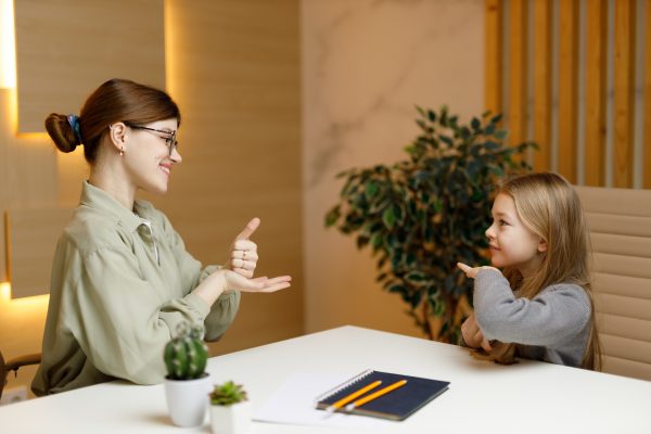Woman teacher and girl child communicate in sign language, elementary school.